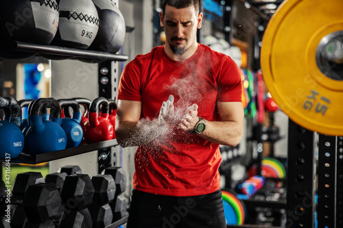 Weightlifter clapping hands and preparing for workout at a gym. Focus on white powder dust. A man stands in the gym between workout equipments and prepares to lift weights photo