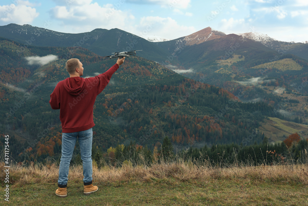 Young man with modern drone in mountains, back view. Space for text