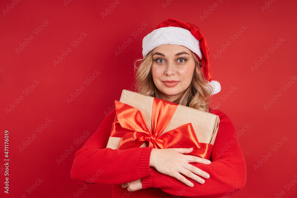 Lovely Santa woman in cap holding christmas present tied with ribbon isolated on red background Lovely Santa woman in cap holding christmas present tied with ribbon isolated on red background