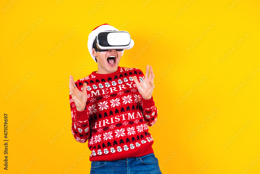 young latin man gamer in virtual reality headset gadget wearing Santa hat and Christmas sweater on yellow background. Christmas and winter vr technology concept in Mexico Latin America young latin man gamer in virtual reality headset gadget wearing Santa hat and Christmas sweater on yellow background. Christmas and winter vr technology concept in Mexico Latin America