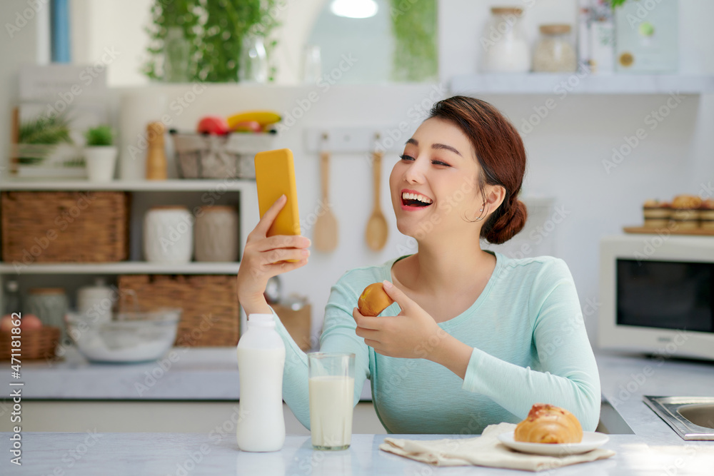 Smiling pretty asian young woman surfing on Internet while having healthy breakfast at home.