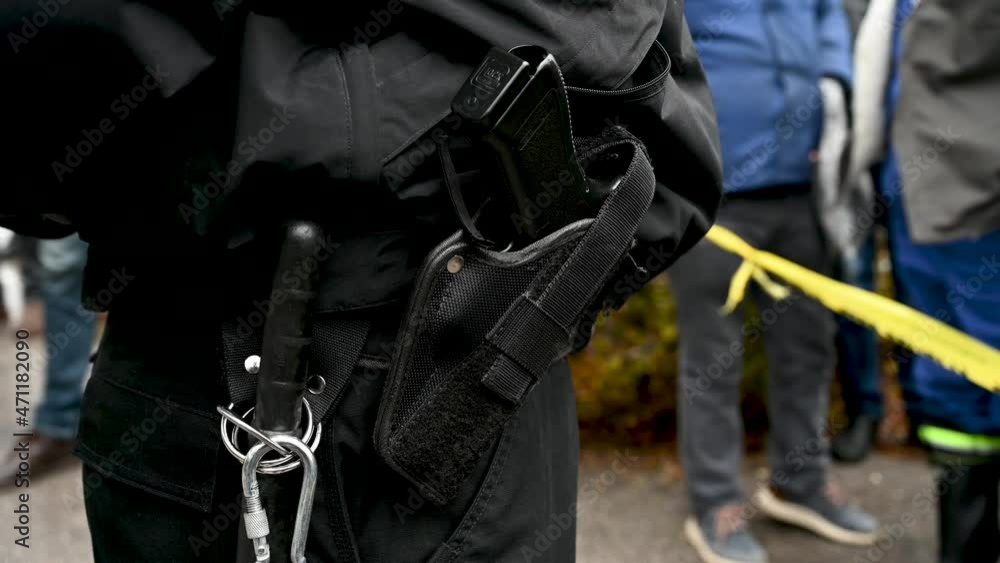 Police officer's belt with a gun and baton tonfa. Policeman standing on the street during protest. Policeman carrying pistol weapon in holster on demonstration. Police officer's belt with a gun and baton tonfa. Policeman standing on the street during protest. Policeman carrying pistol weapon in holster on demonstration.
