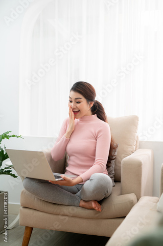 Beautiful of portrait asian young woman excited and glad of success with laptop on sofa