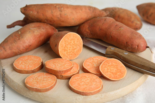 Whole and cut ripe sweet potatoes on white wooden table