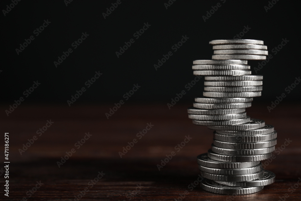 Many coins stacked on wooden table against black background, space for text Many coins stacked on wooden table against black background, space for text