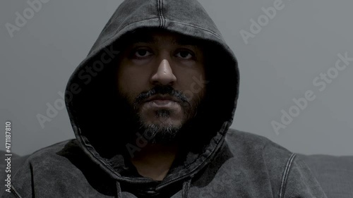 Close up dolly shot of the face of an Indian man wearing a hoodie, his eyes fixed in an intense determined stare while remaining completely motionless
