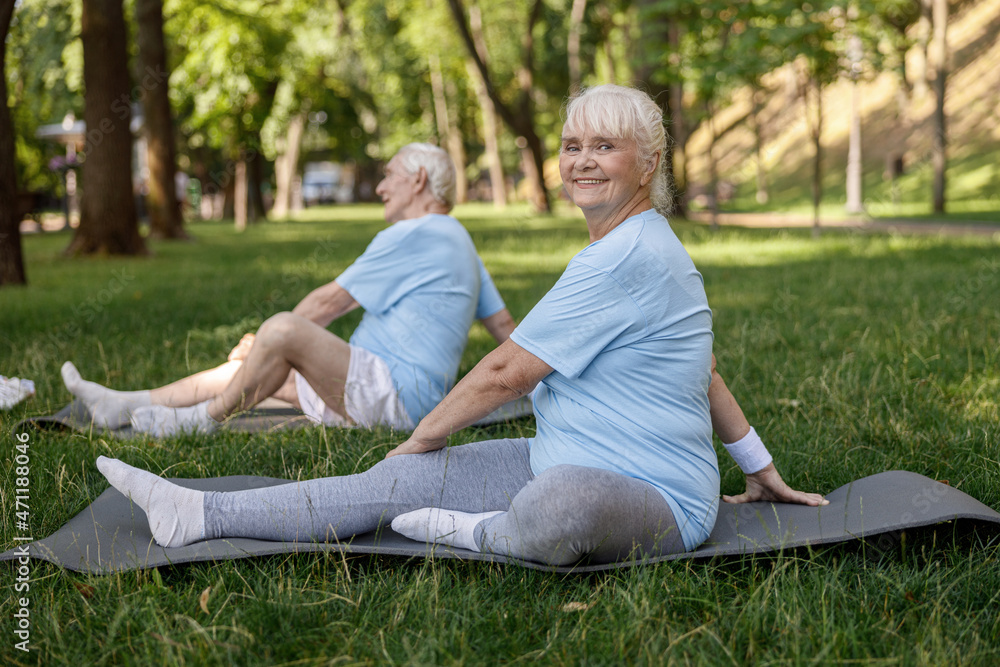 Positive mature woman with friend do yoga asanas on field grass in picturesque park Positive mature woman with friend do yoga asanas on field grass in picturesque park
