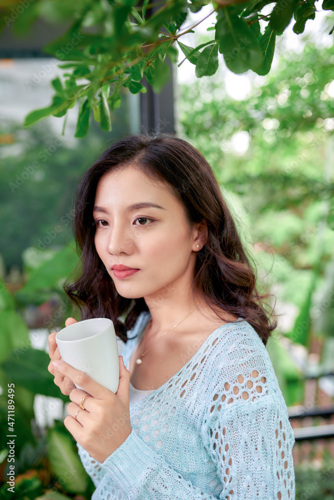 Hanging potted plants in summer with woman standing on porch of house in morning wooden cabin cottage drinking tea or coffee Hanging potted plants in summer with woman standing on porch of house in morning wooden cabin cottage drinking tea or coffee