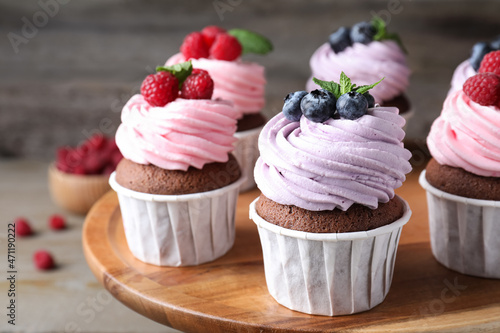 Sweet cupcakes with fresh berries on wooden plate, closeup
