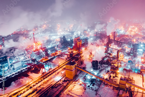Fototapeta Naklejka Na Ścianę i Meble -  Aerial view of steel plant at night with smokestacks and fire blazing out of the pipe. Industrial panoramic landmark with blast furnance of metallurgical production. Concept of environmental pollution