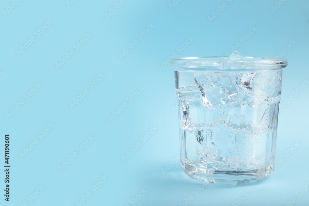 Glass of soda water with ice on light blue background. Space for text Glass of soda water with ice on light blue background. Space for text