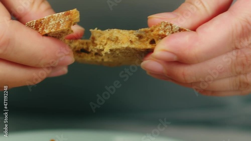 Woman breaks off piece of whole-grain rye bread with hands to eat with stewed chicken and vegetables extreme closeup slow motion photo