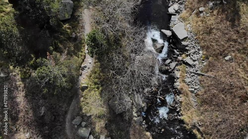 Aerial: zenital shot of a river and a path with hikers in the mountains. Following the course of the river photo
