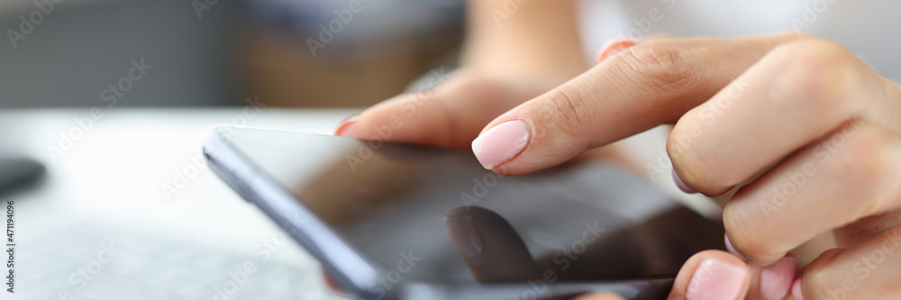 Girl presses finger on screen of smartphone on table is laptop Girl presses finger on screen of smartphone on table is laptop