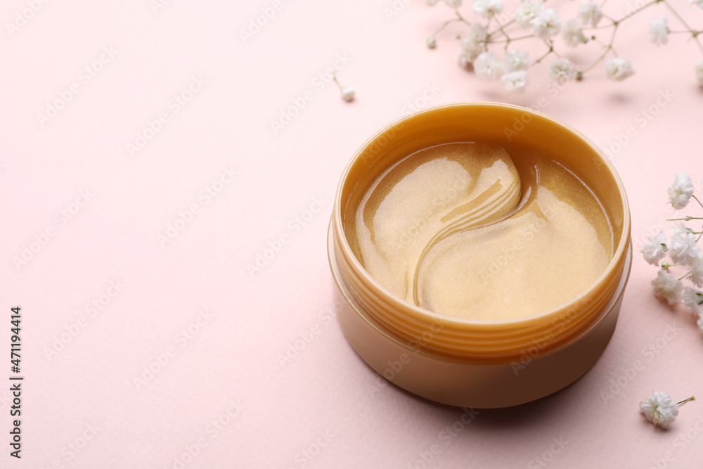 Under eye patches in jar and flowers on light pink background, space for text. Cosmetic product Under eye patches in jar and flowers on light pink background, space for text. Cosmetic product
