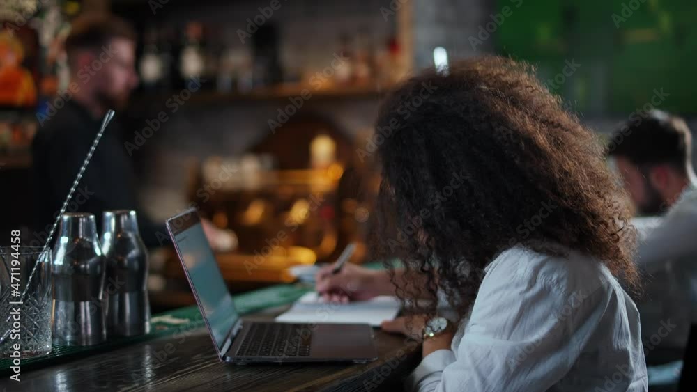 Female freelancer works outside the home, female developer sits at the bar and works at a laptop, writes in a notebook. Female freelancer works outside the home, female developer sits at the bar and works at a laptop, writes in a notebook.
