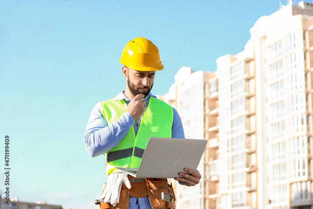 Thoughtful construction worker using laptop outdoors Thoughtful construction worker using laptop outdoors