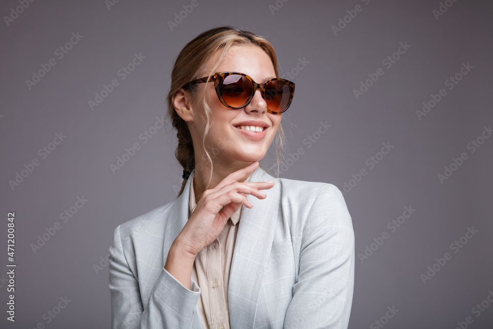 Fashion photo of a beautiful elegant young woman in a pretty soft blue suit, jacket, pants, trousers, white boots, stylish sunglasses on light gray background. Studio shot, portrait. Monochrome colors Fashion photo of a beautiful elegant young woman in a pretty soft blue suit, jacket, pants, trousers, white boots, stylish sunglasses on light gray background. Studio shot, portrait. Monochrome colors
