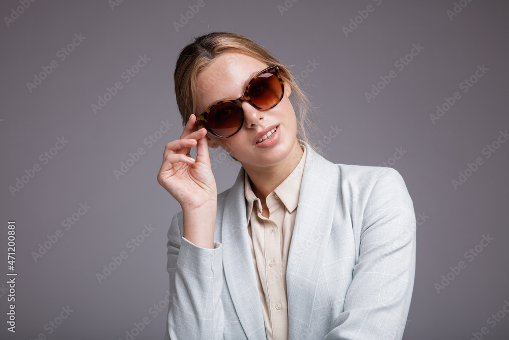 Fashion photo of a beautiful elegant young woman in a pretty soft blue suit, jacket, pants, trousers, white boots, stylish sunglasses on light gray background. Studio shot, portrait. Monochrome colors Fashion photo of a beautiful elegant young woman in a pretty soft blue suit, jacket, pants, trousers, white boots, stylish sunglasses on light gray background. Studio shot, portrait. Monochrome colors