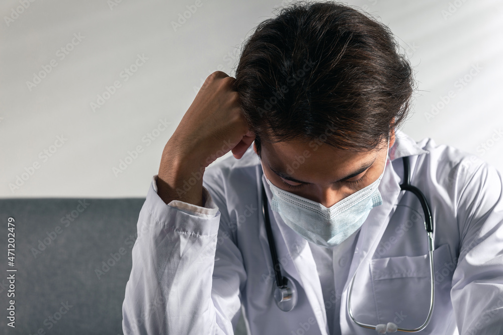 Depressed Young Asian male doctor with surgery face mask in a medical coat Overworked having a mental health breakdown during covid-19 outbreak. Medical and coronavirus Stress and frustration concept Depressed Young Asian male doctor with surgery face mask in a medical coat Overworked having a mental health breakdown during covid-19 outbreak. Medical and coronavirus Stress and frustration concept