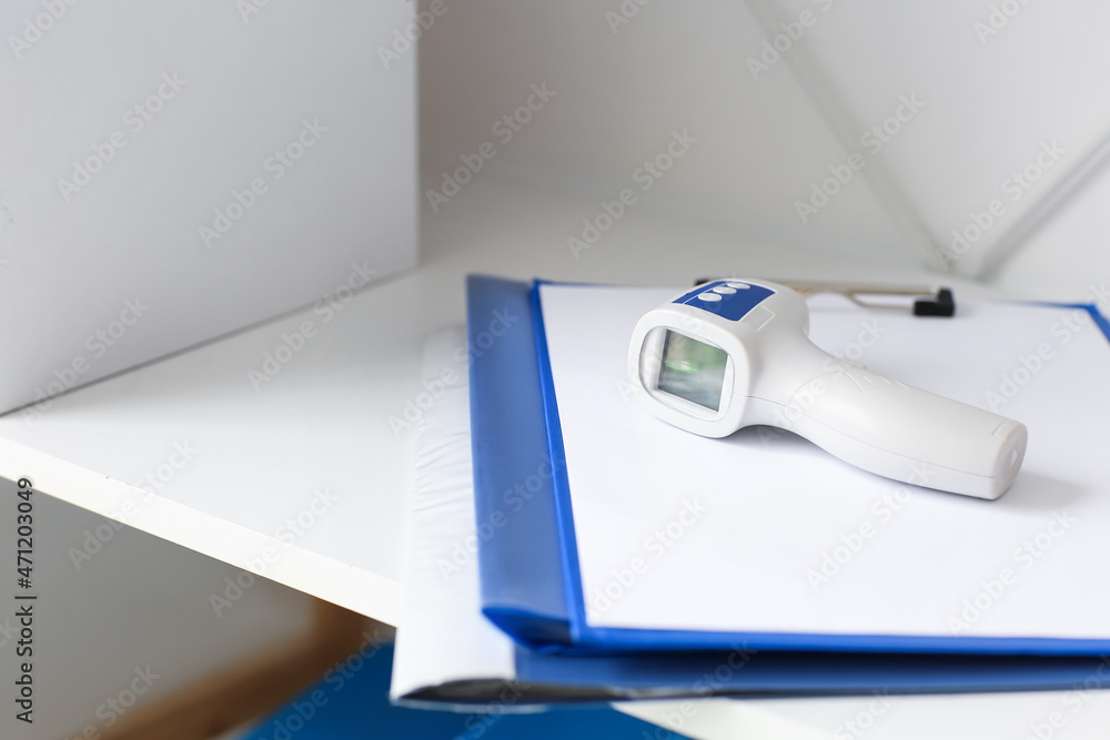 Infrared thermometer and clipboard on shelf in medical office, closeup Infrared thermometer and clipboard on shelf in medical office, closeup