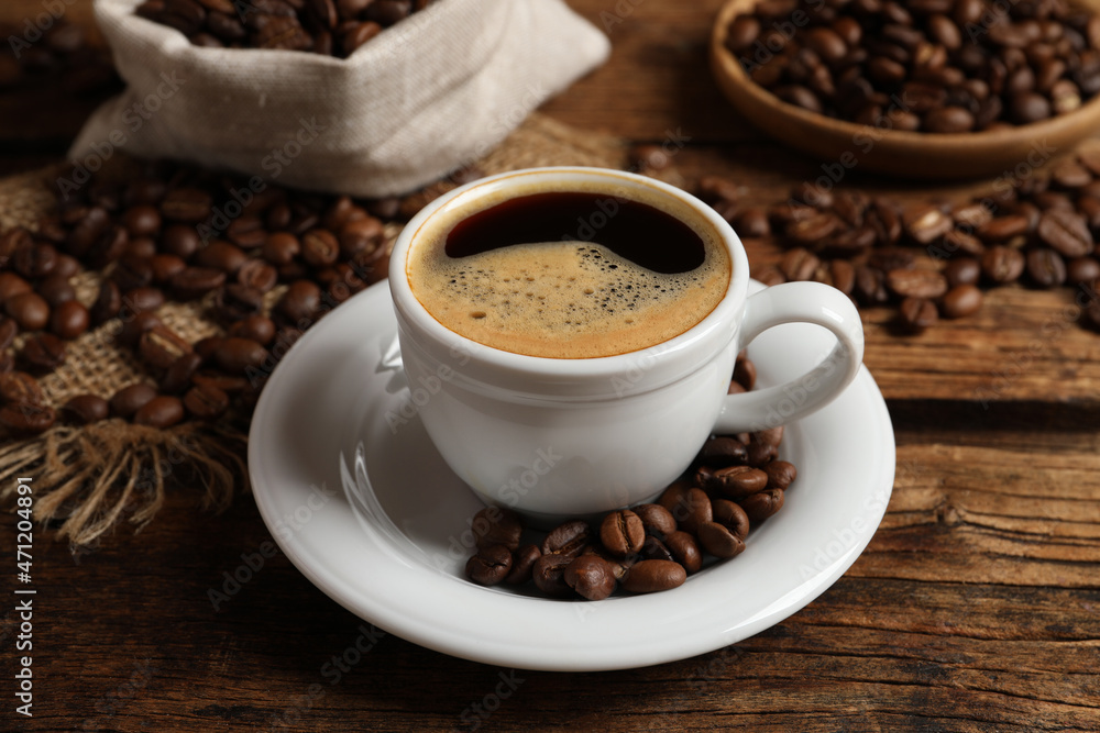 Cup of aromatic hot coffee and beans on wooden table Cup of aromatic hot coffee and beans on wooden table