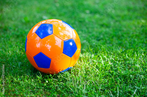Close up of bright orange and blue football ball on a green grass. Football section for children concept.