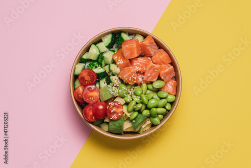 Salmon, avocado, cucumber, tomato, edamame beans and rice poke bowl on pink yellow background