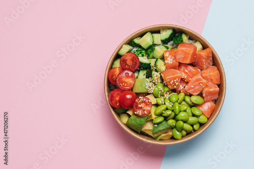 Salmon, avocado, cucumber, tomato, edamame beans and rice poke bowl on pink blue background photo