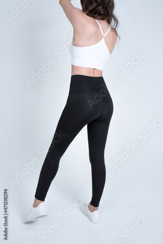 slender legs in black pants leggings on a light background. woman in sports clothes.