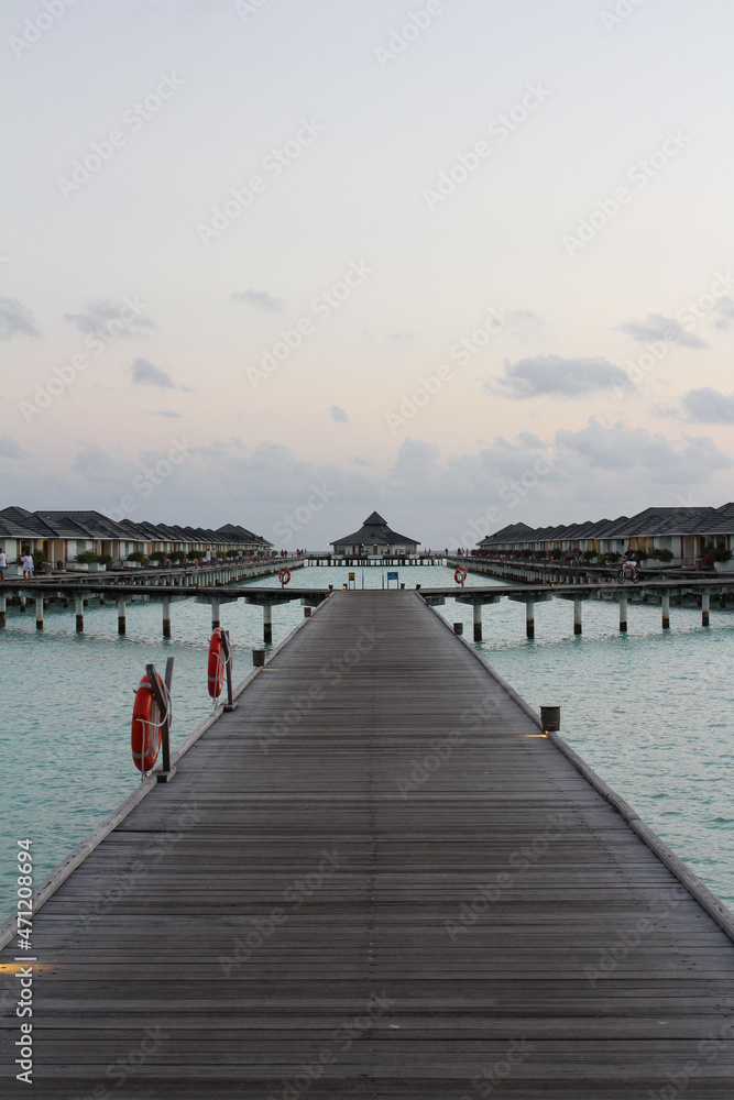 Wooden pier with lifebuoys leading to villas on stilts above the water in the Maldives.