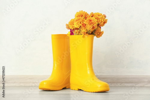 Pair of yellow rubber boots and chrysanthemum flowers against light wall