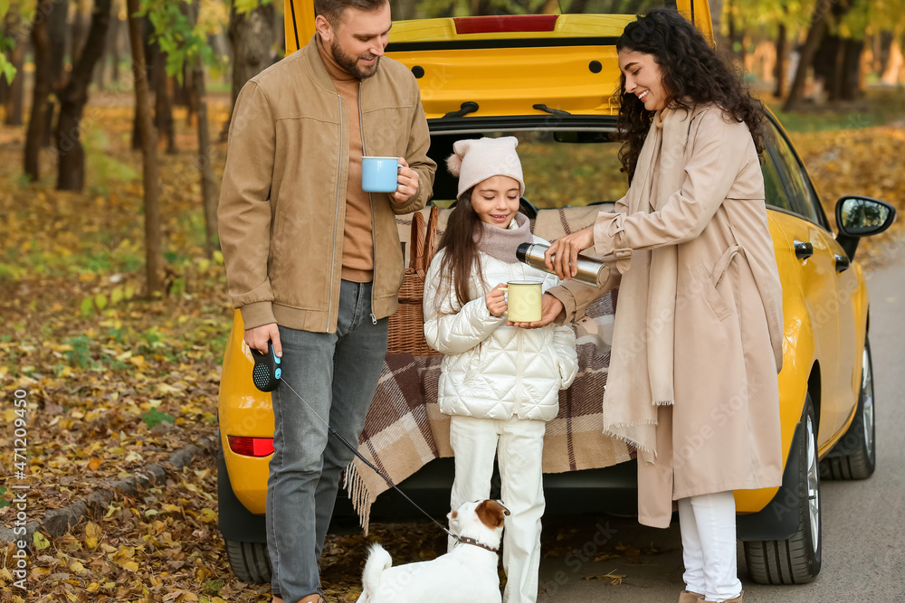 Fototapeta premium Happy family with cute dog drinking hot tea near yellow car on autumn day