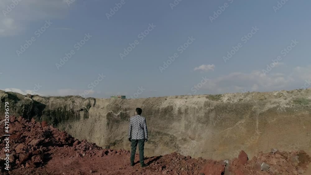Back view of young man in original costume and gloves standing on high mountain and looking around . Great canyon beautiful scene . Alien land , abandoned desert . Drone camera moving in slow motion Back view of young man in original costume and gloves standing on high mountain and looking around . Great canyon beautiful scene . Alien land , abandoned desert . Drone camera moving in slow motion