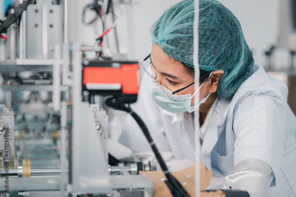 Both male and female Asian scientists are outfitted with protective gear. Examining the factory's machinery and materials used in the mask-making process. Covid 19 is a piece of preventive equipment.