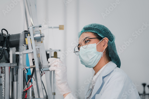 Both male and female Asian scientists are outfitted with protective gear. Examining the factory's machinery and materials used in the mask-making process. Covid 19 is a piece of preventive equipment.