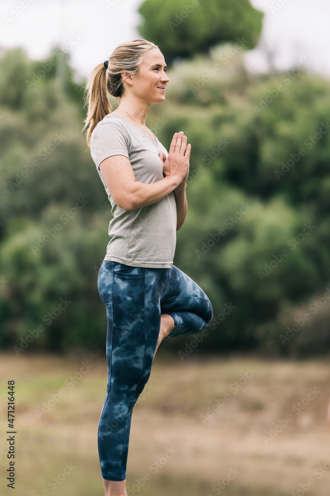 Woman standing doing yoga outside surrounded by nature Woman standing doing yoga outside surrounded by nature