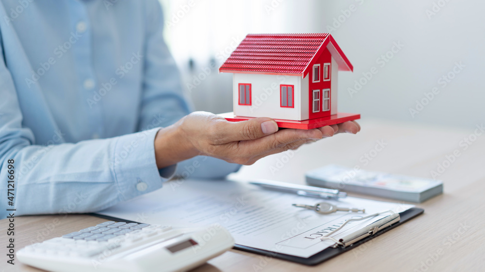 The real estate concept the realtor presenting his work towards his customer by putting the red house model on his palms and raising his hands a little The real estate concept the realtor presenting his work towards his customer by putting the red house model on his palms and raising his hands a little