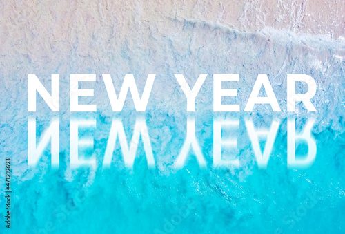 The word new year written by the ocean with a wave on the beach. Background for advertising 