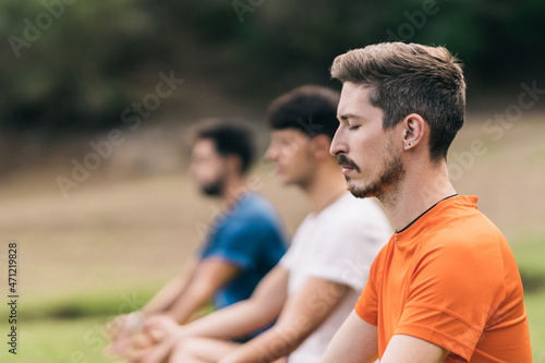 Three men practising the yoga lotus position in a park