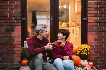A couple having a romantic date on the porch of their home. Cozy ideas on how to spend time at home. Autumn tea time outdoors on house entrance decorated with pumpkins, flowers and burning candles