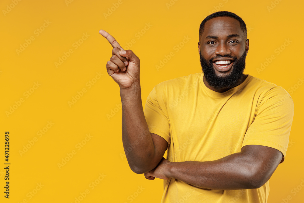 Young smiling happy black man 20s wearing bright casual t-shirt point index finger aside on workspace area mock up isolated on plain yellow color background studio portrait. People lifestyle concept. Young smiling happy black man 20s wearing bright casual t-shirt point index finger aside on workspace area mock up isolated on plain yellow color background studio portrait. People lifestyle concept.