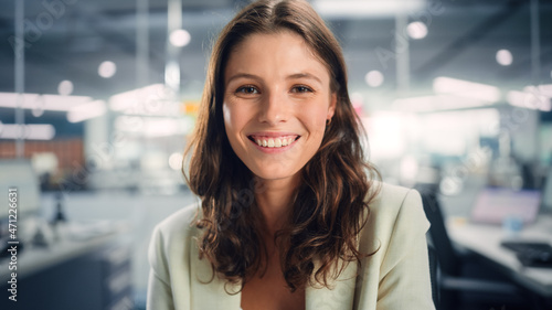 Portrait of a Beautiful Happy Young Female Wearing White Jacket, Looking at Camera, Posing and Charmingly Smiling. Successful Brunette Woman with Brown Eyes Working in Diverse Company Office.