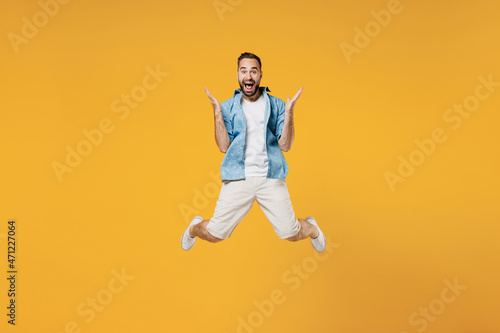 Full body young surprised overjoyed excited happy caucasian man 20s wear blue shirt white t-shirt jump high spread hands isolated on plain yellow background studio portrait. People lifestyle concept.