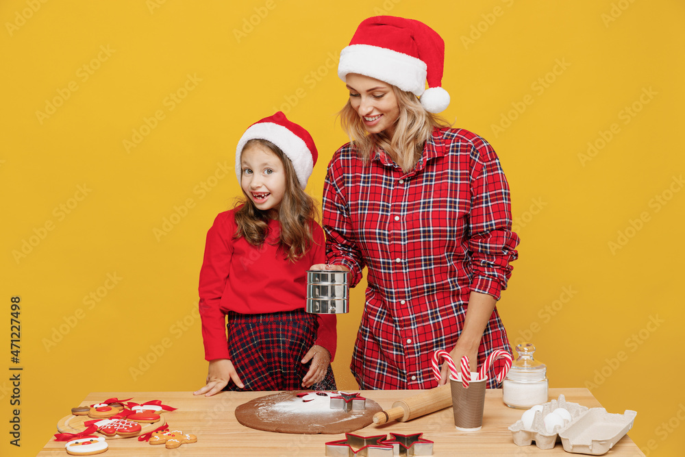 Two woman mother fun child baby girl in red Christmas hat isolated on plain yellow wall background studio. Mom little kid cook ginger cookie at kitchen table home. Happy New Year 2022 holiday concept Two woman mother fun child baby girl in red Christmas hat isolated on plain yellow wall background studio. Mom little kid cook ginger cookie at kitchen table home. Happy New Year 2022 holiday concept