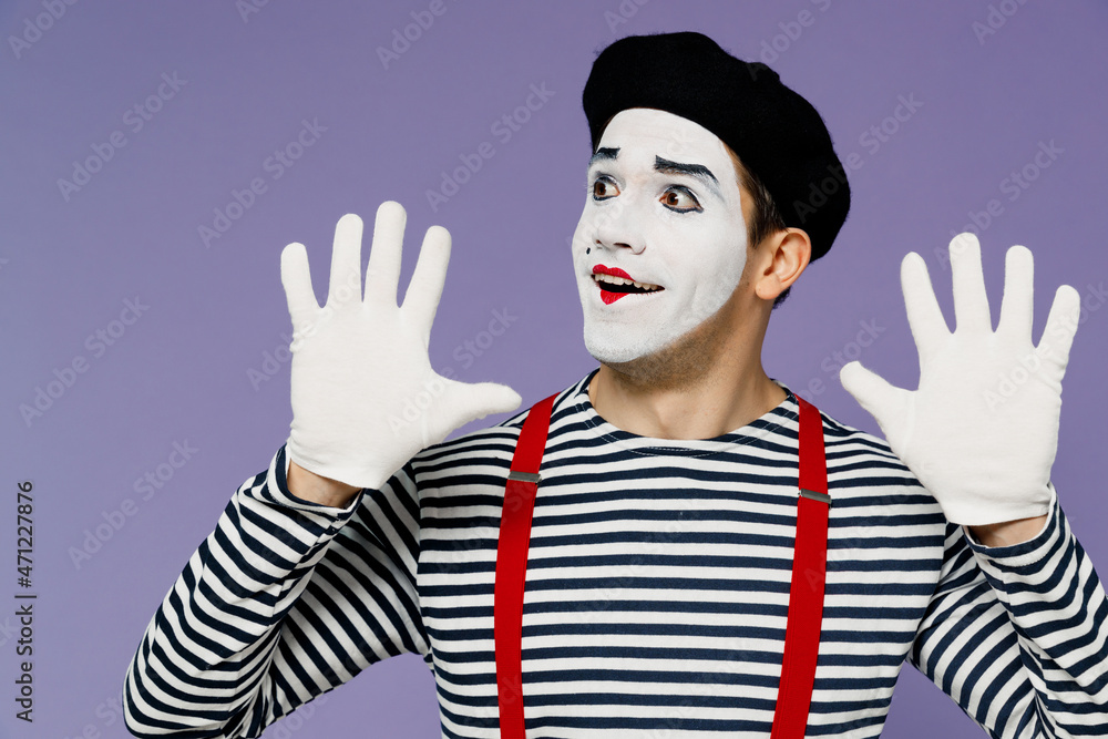 Astonished young mime man with white face mask wears striped shirt beret holding palms up like touching imaginary wall looking aside isolated on plain pastel light violet background studio portrait. Astonished young mime man with white face mask wears striped shirt beret holding palms up like touching imaginary wall looking aside isolated on plain pastel light violet background studio portrait.
