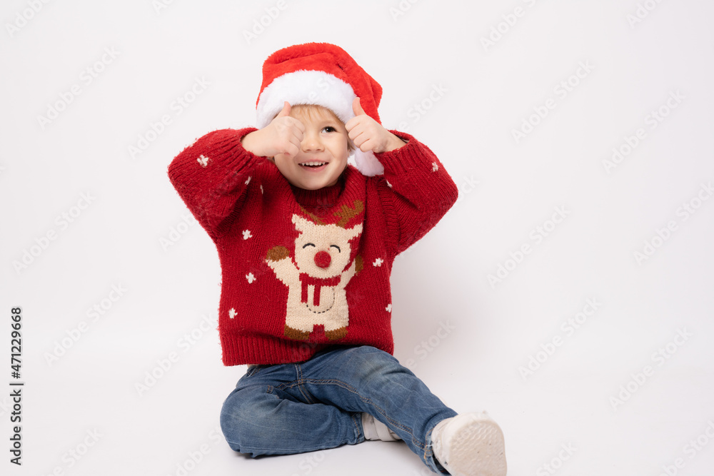 Little boy wearing santa hat sitting on floor with thumbs up isolated over white background. Little boy wearing santa hat sitting on floor with thumbs up isolated over white background.