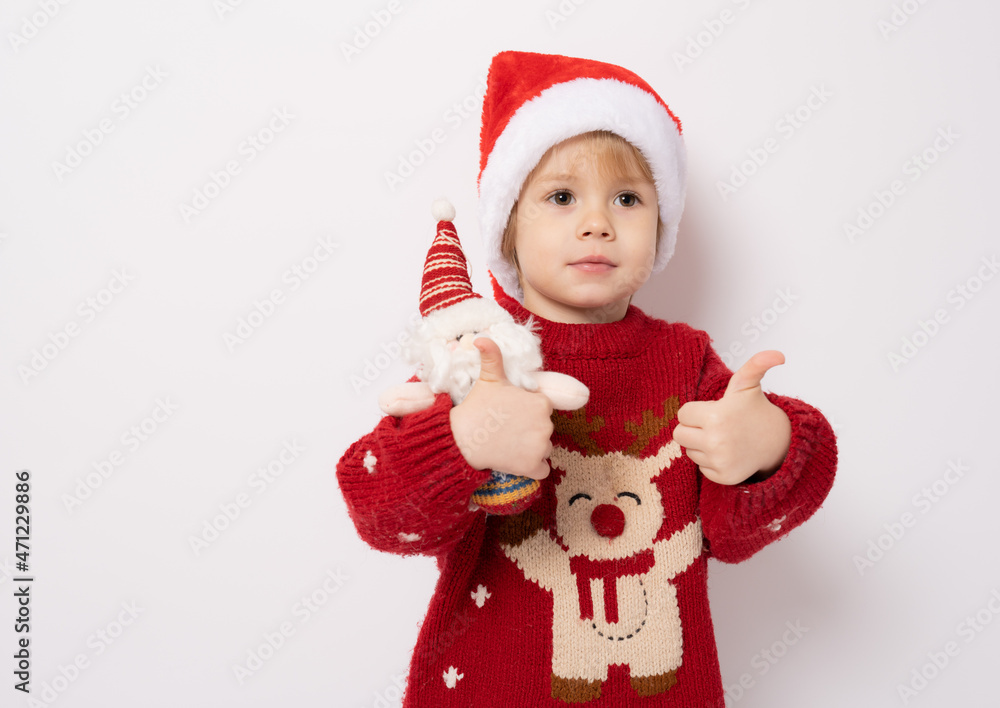 Little boy wearing santa hat holding santa claus toy with thumb up standing over white background. Little boy wearing santa hat holding santa claus toy with thumb up standing over white background.