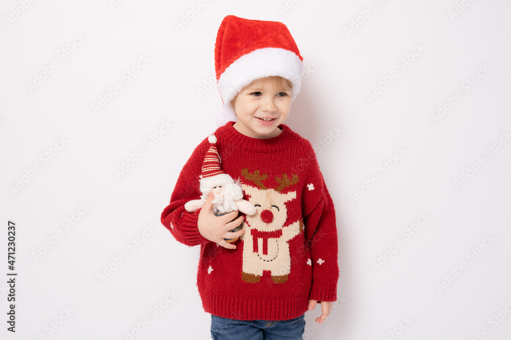 Little boy wearing santa hat holding santa claus toy standing over white background. Little boy wearing santa hat holding santa claus toy standing over white background.