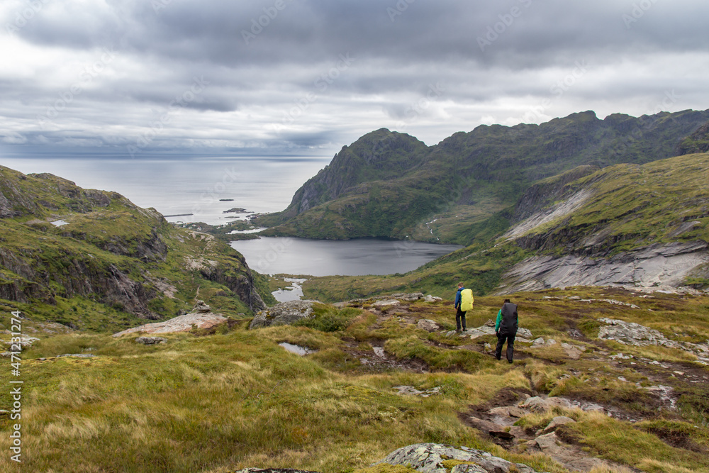 Two hiker with big backpacks on a path near a fjord on Lofoten islands with dramatic cloudy sky